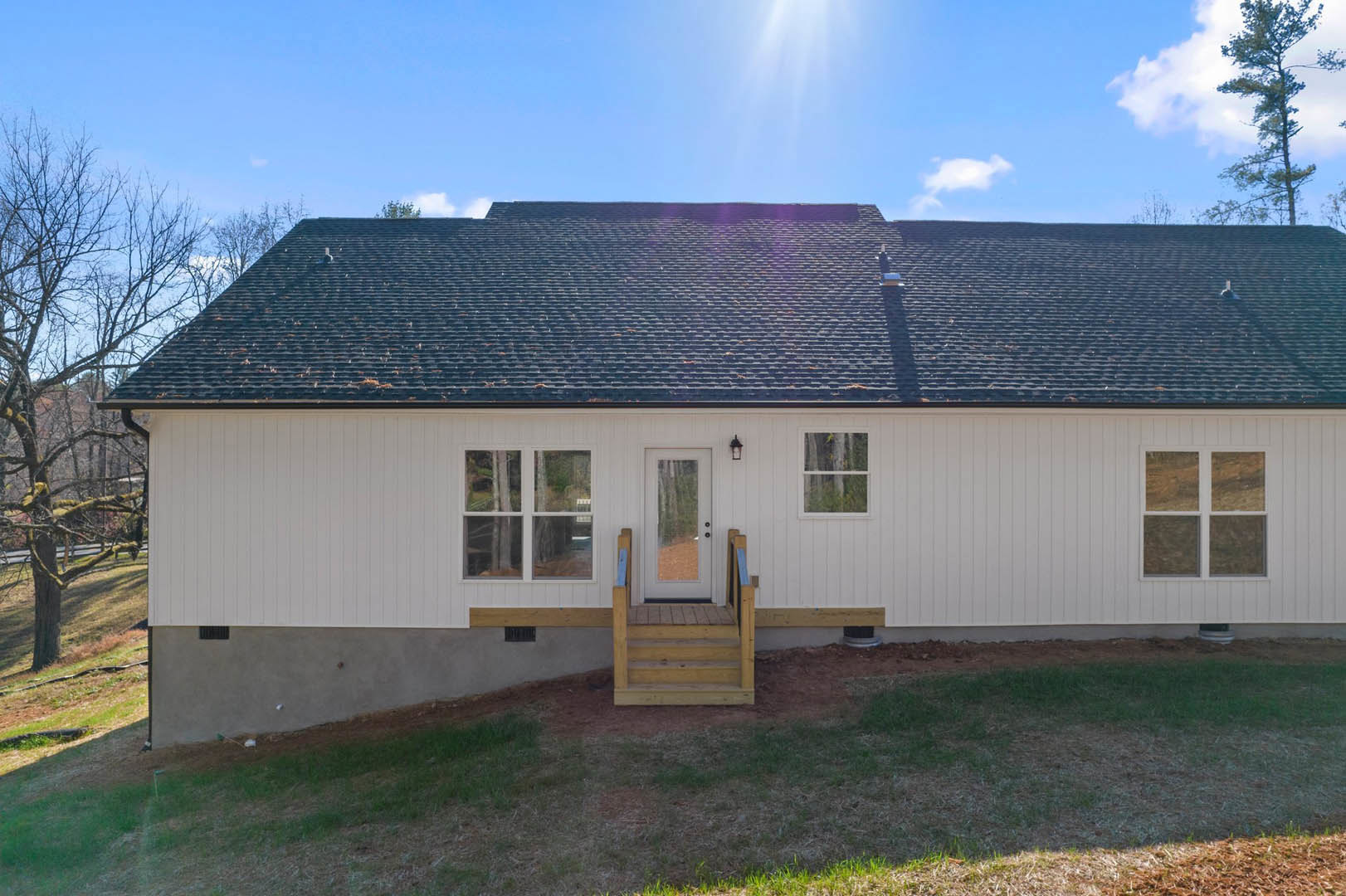 White cottage-style home with two covered porches, wooden steps leading to front door, large windows, gabled roof, surrounded by green lawn and mature trees under partly cloudy sky