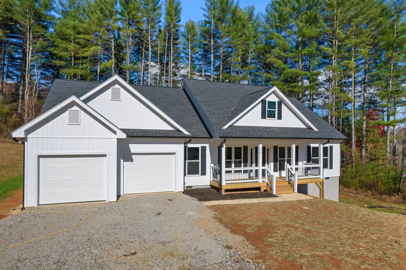 Two-story house with light siding, covered porch, wooden deck, paved driveway, white-framed windows, and mature trees in the background
