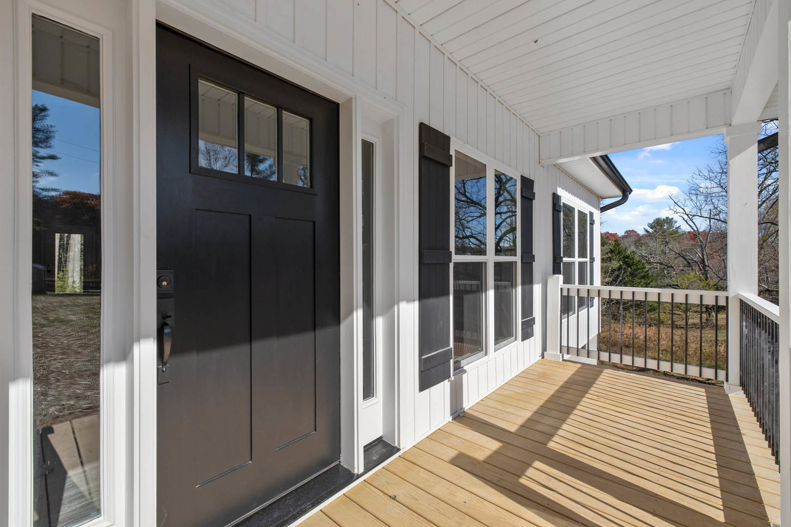 Front porch with wooden deck, black door and handle, white paneled ceiling, close-up window, white railing with black bars