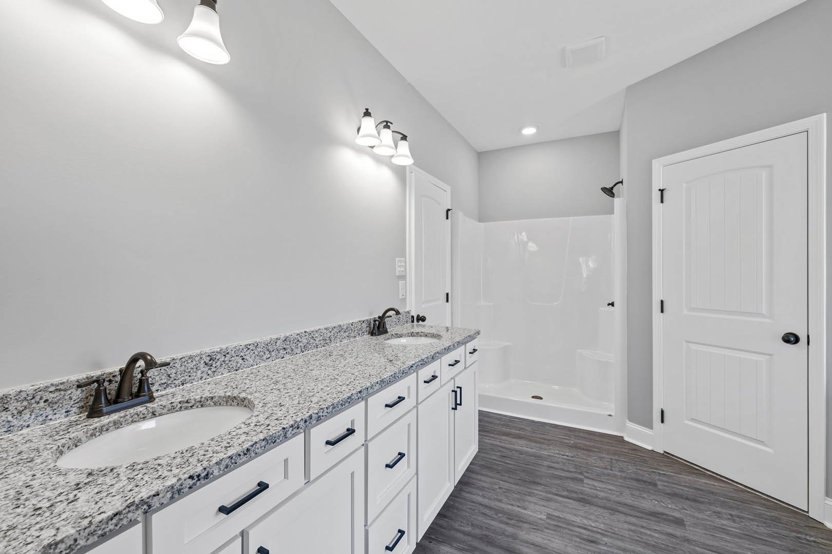 Bathroom featuring white cabinetry, marble countertops, undermount sink with chrome faucet, three-light fixture above mirror, white door with black hardware, and tiled walls.