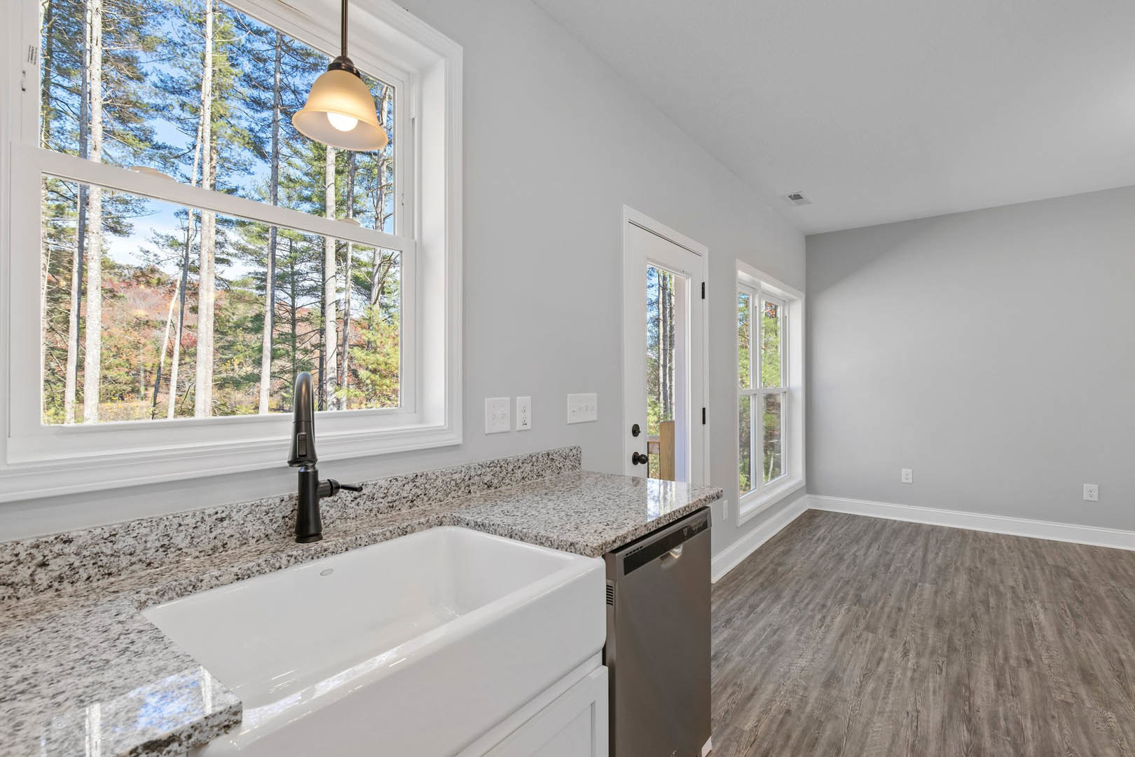 Open kitchen with tile backsplash, stainless steel sink, built-in dishwasher, and window overlooking trees