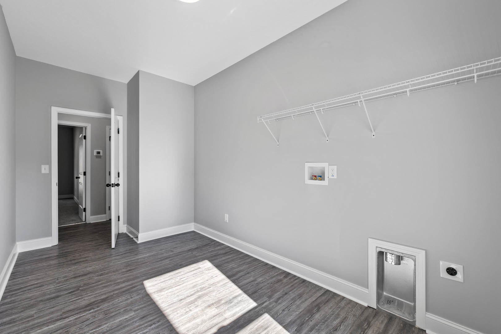 Wood plank flooring, white plaster wall, white metal shelf, black electrical outlet, water dispenser, door with white trim