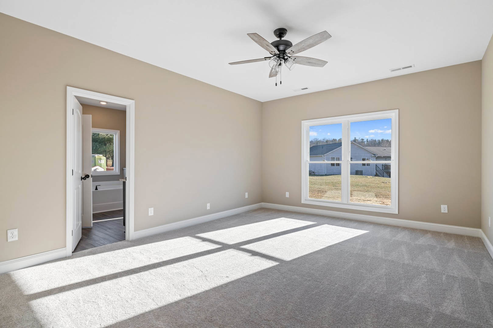 Ceiling fan with glass light fixtures, white carpeted floor, large window with view of neighboring house, white walls, and plaster ceiling