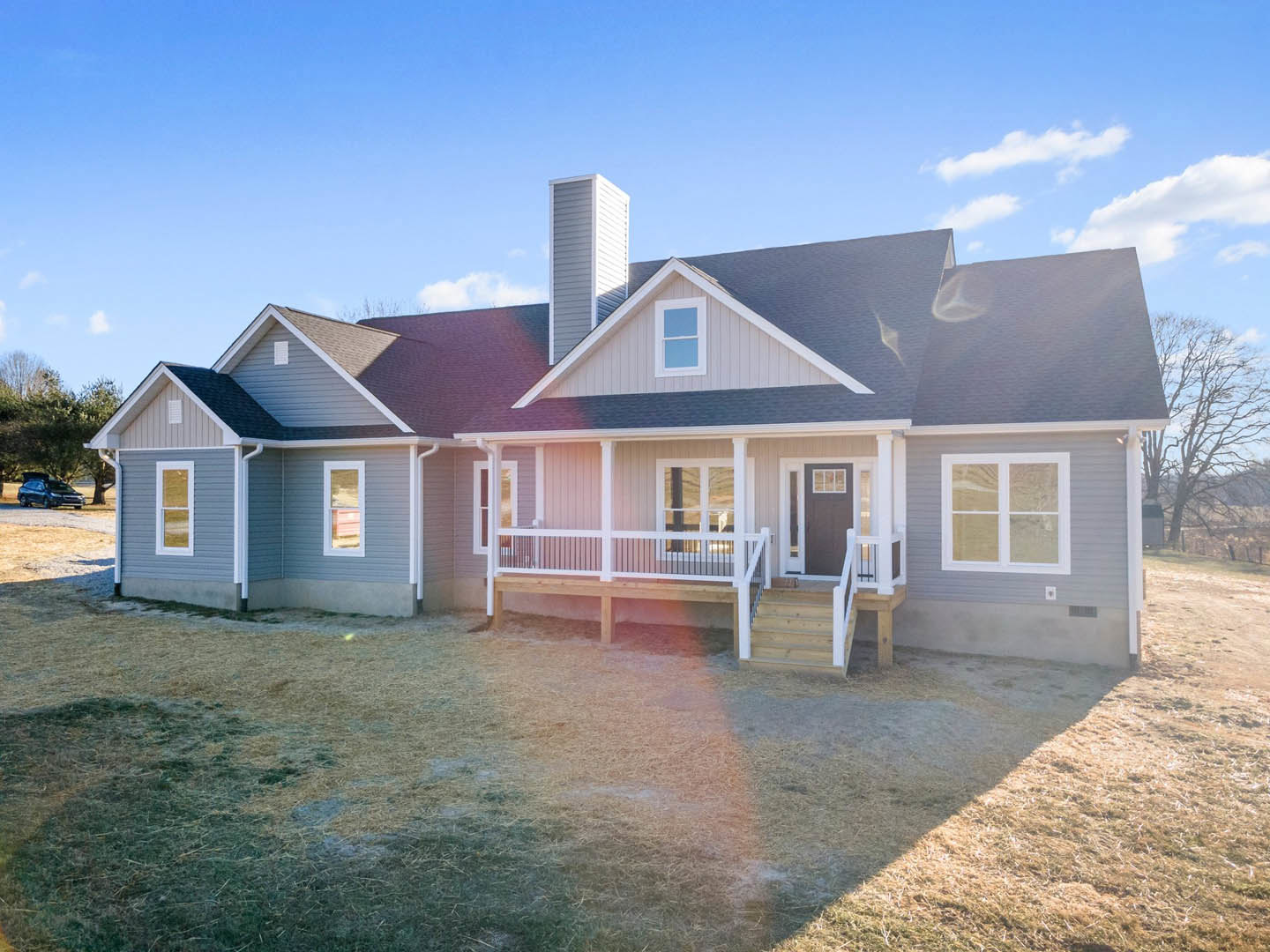 Two-story home with white siding, covered front porch, brick chimney, manicured lawn, white-framed windows, and blue sky with scattered clouds
