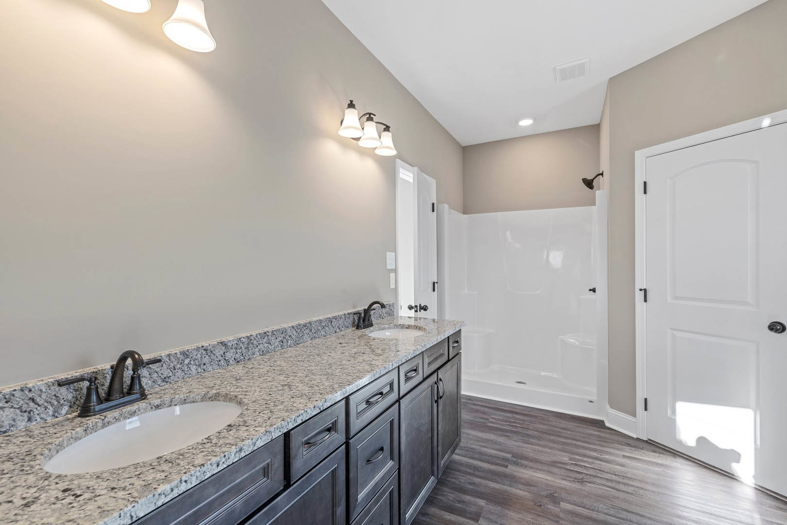 Bathroom featuring a marble countertop with undermount sink, chrome faucet, white cabinetry, glass-enclosed shower with tile walls, black door handle, and three-light fixture above