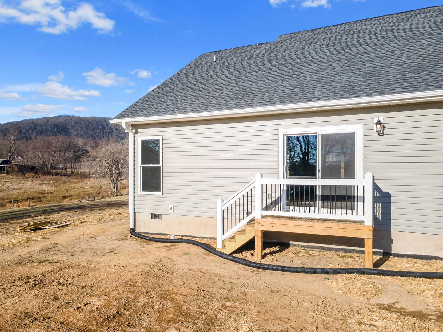 Wooden deck with white railing and stairs leading to a porch, white-framed window, dark roof, hose on the ground, tree silhouettes against evening sky