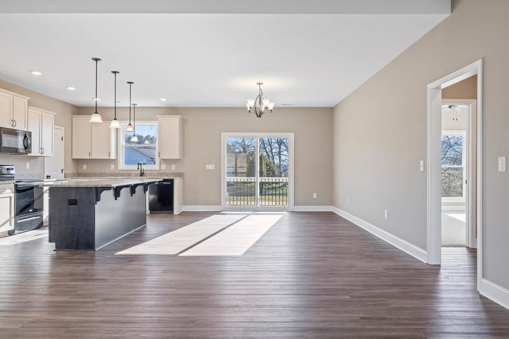 Open-concept kitchen with wood laminate flooring, white cabinetry, stone countertops, kitchen island, stainless steel microwave, modern chandelier, sliding glass door leading to