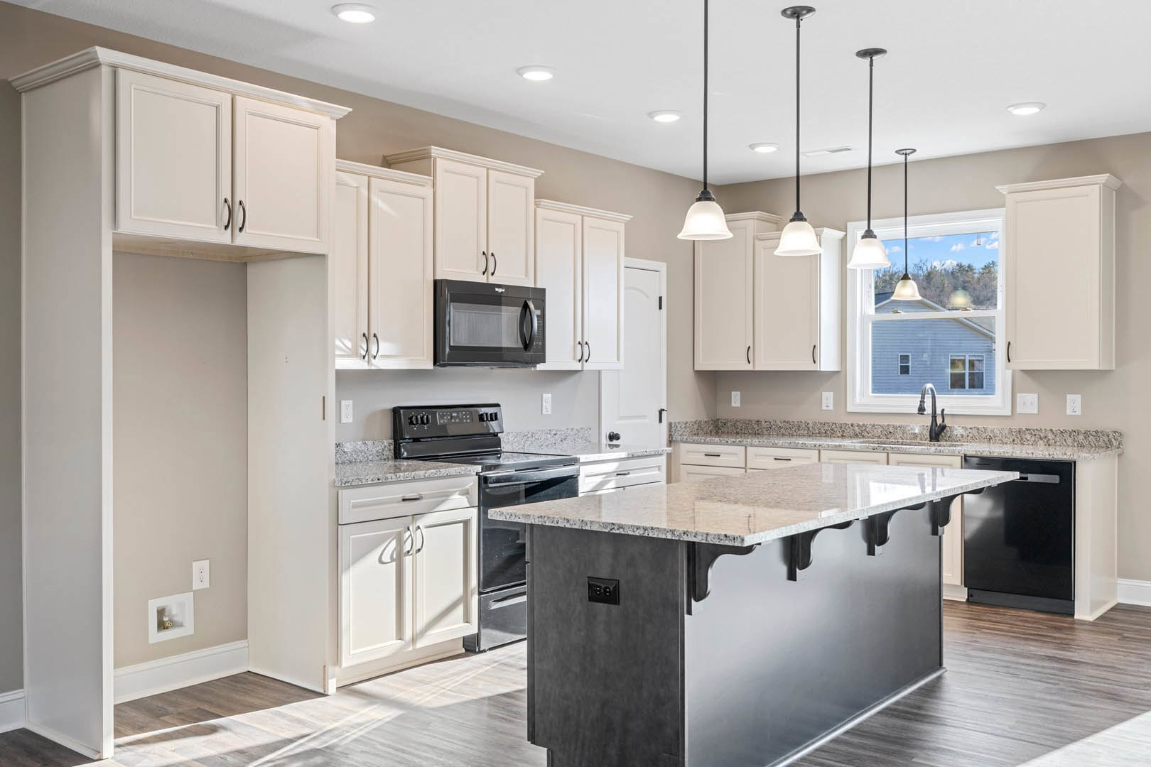 Spacious kitchen featuring a large marble-topped island, white cabinetry, black appliances including oven, microwave, and refrigerator, pendant lamps, recessed ceiling lights, and