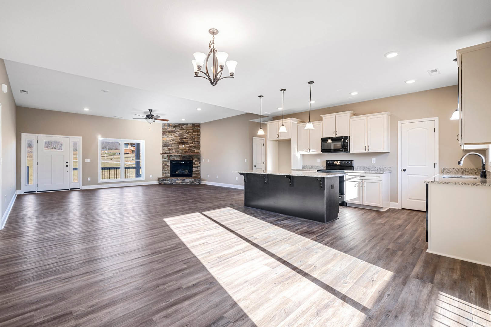 Spacious open floor plan featuring a kitchen with white countertop island, black accent wall, built-in microwave, wood and laminate flooring, stone fireplace, large window