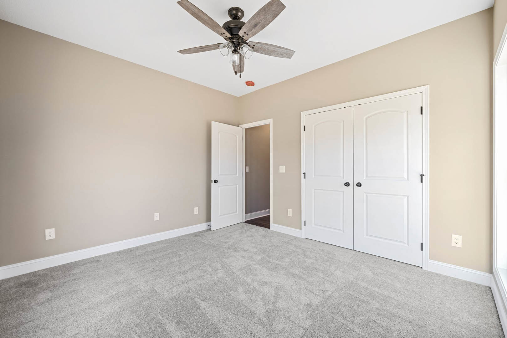 Carpeted room with white double doors featuring black knobs, ceiling fan with glass light fixture, white walls, and crown molding.