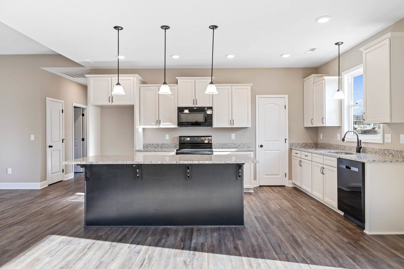 Spacious kitchen featuring a large marble-topped island, white cabinetry with black hardware, stainless steel oven and black microwave, pendant lighting, and light wood flooring.