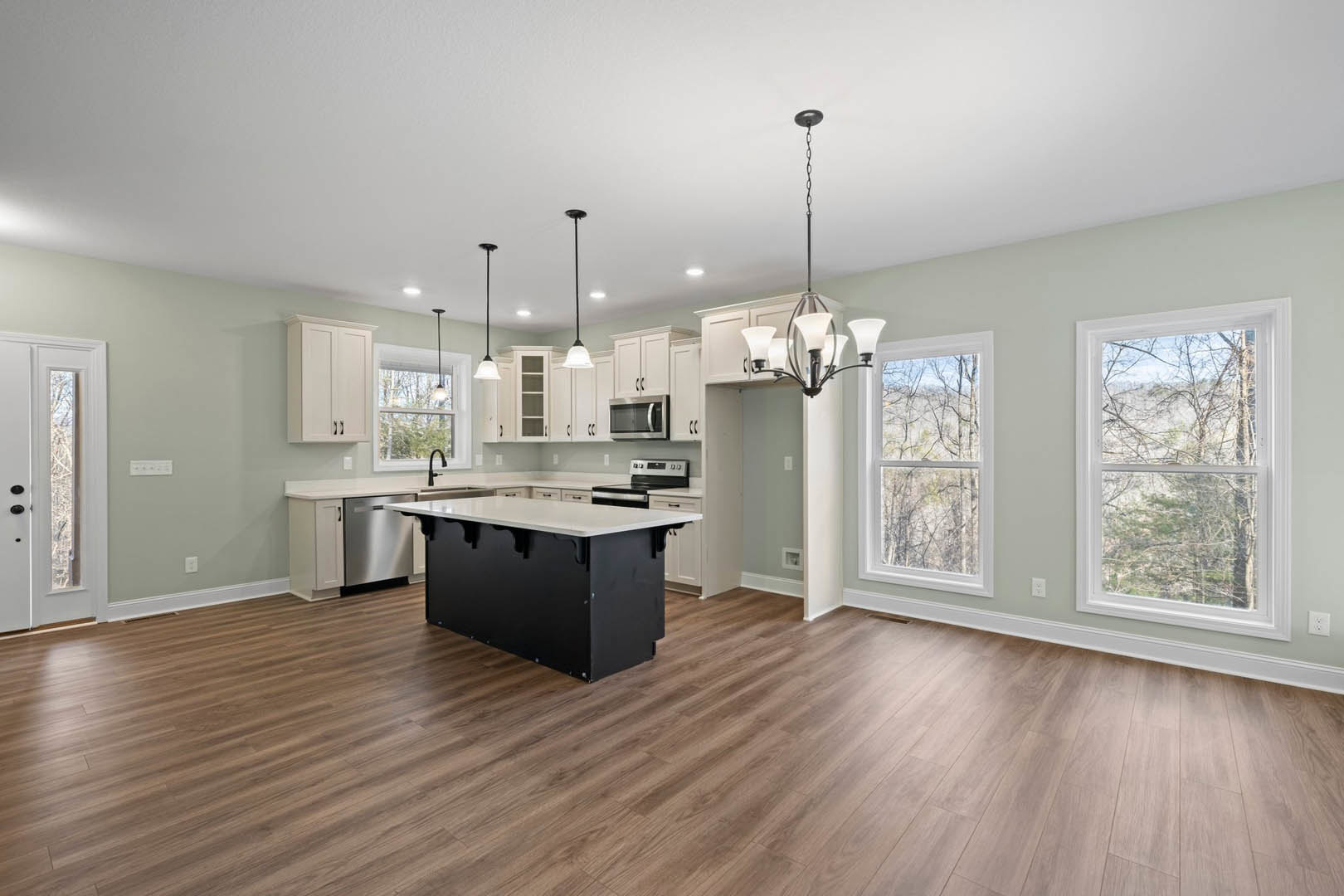 Spacious kitchen featuring a black and white island, wood flooring, white cabinetry, open microwave, black refrigerator, and a window overlooking trees.