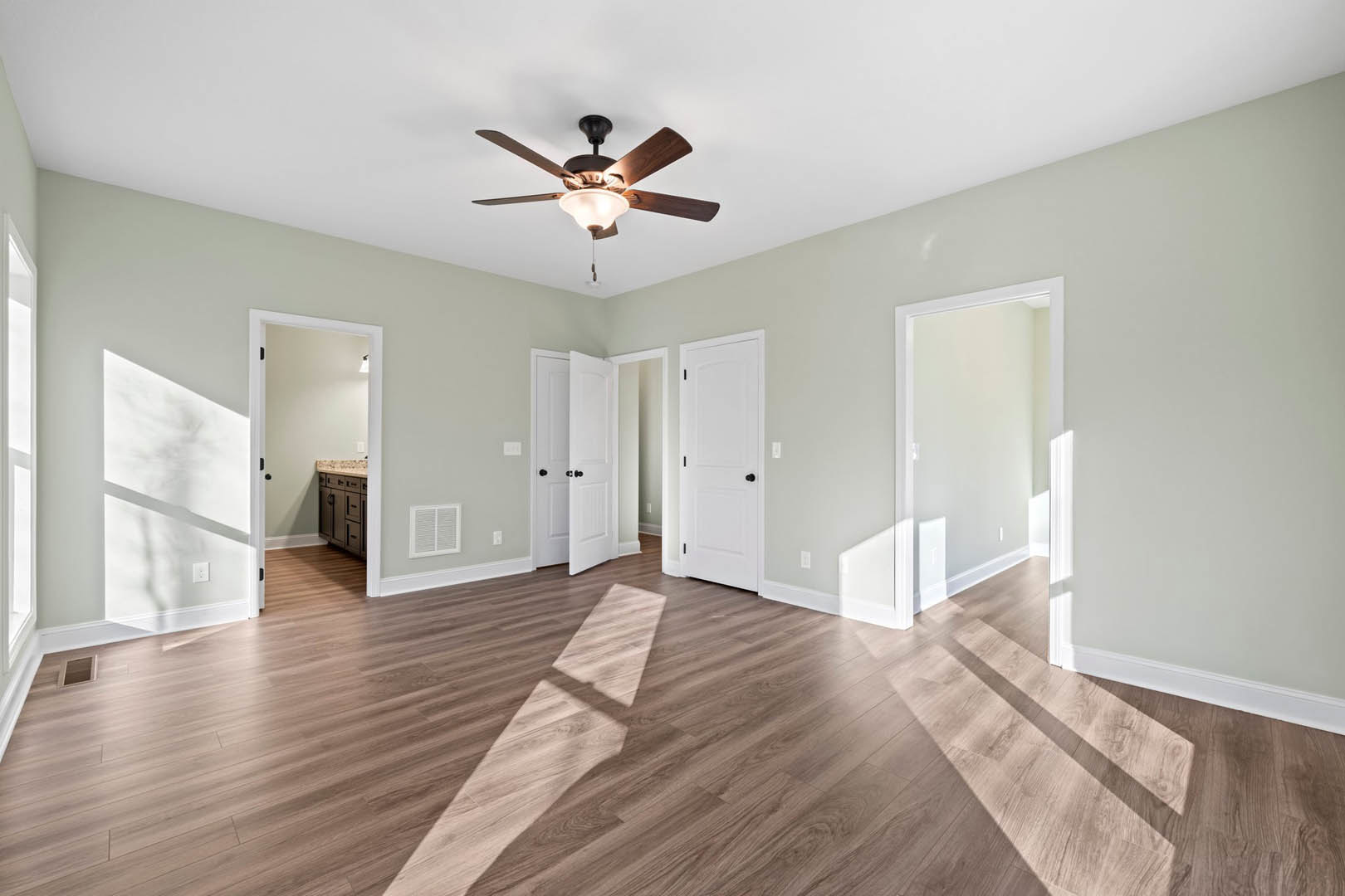 Ceiling fan with light fixture, wood flooring, white walls, white door with black knob, cabinet close-up, baseboard molding