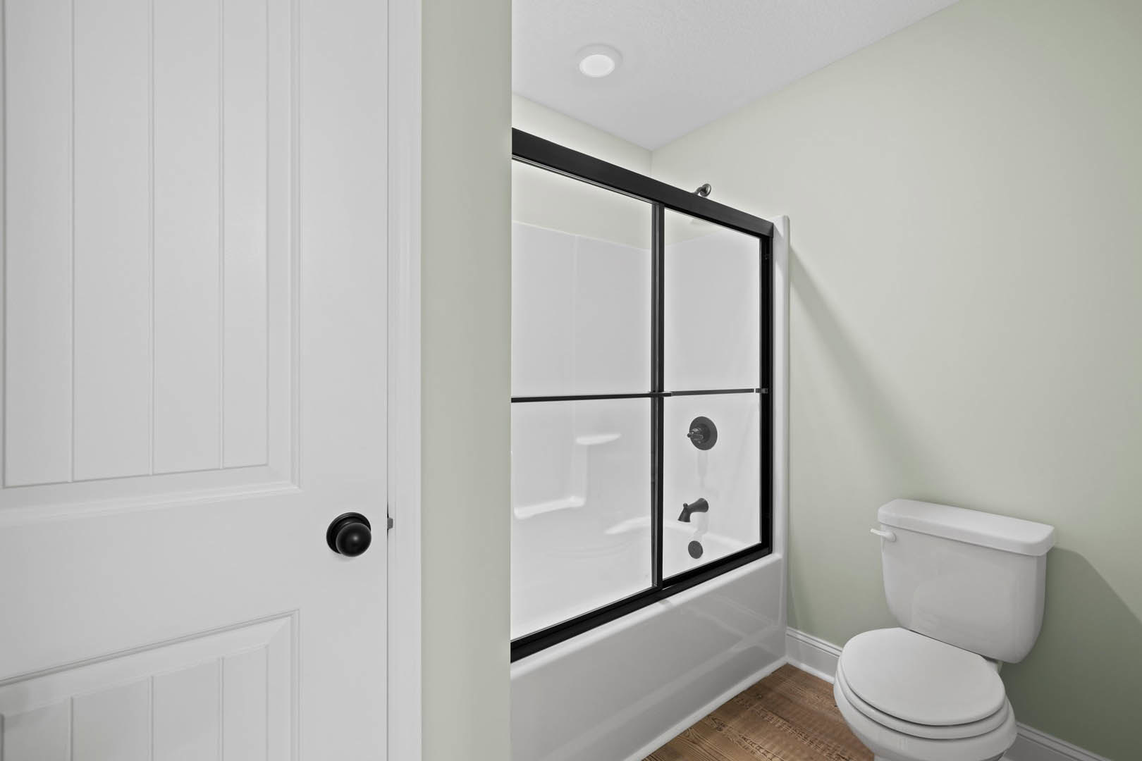 Modern bathroom featuring a glass-enclosed shower, white toilet with closed seat, light-colored tile walls, chrome shower knob, and minimalist fixtures.