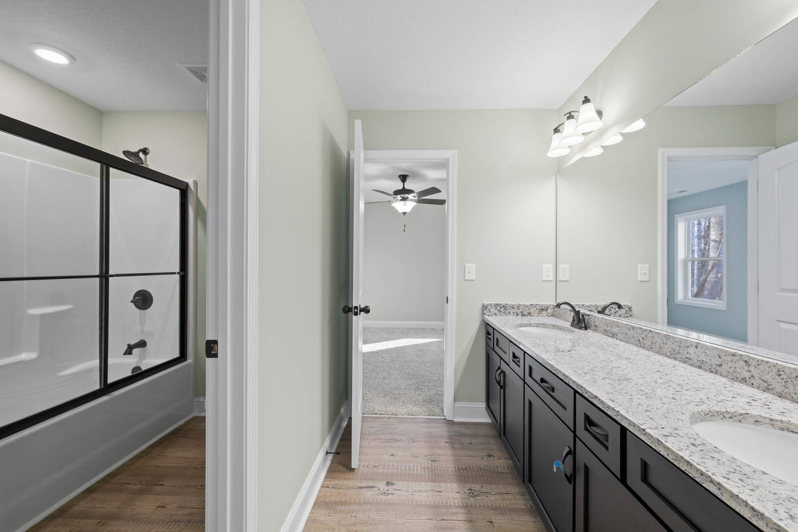 Modern bathroom featuring a glass-enclosed shower, white countertop with undermount sink, black faucet, tiled walls, and a window overlooking trees