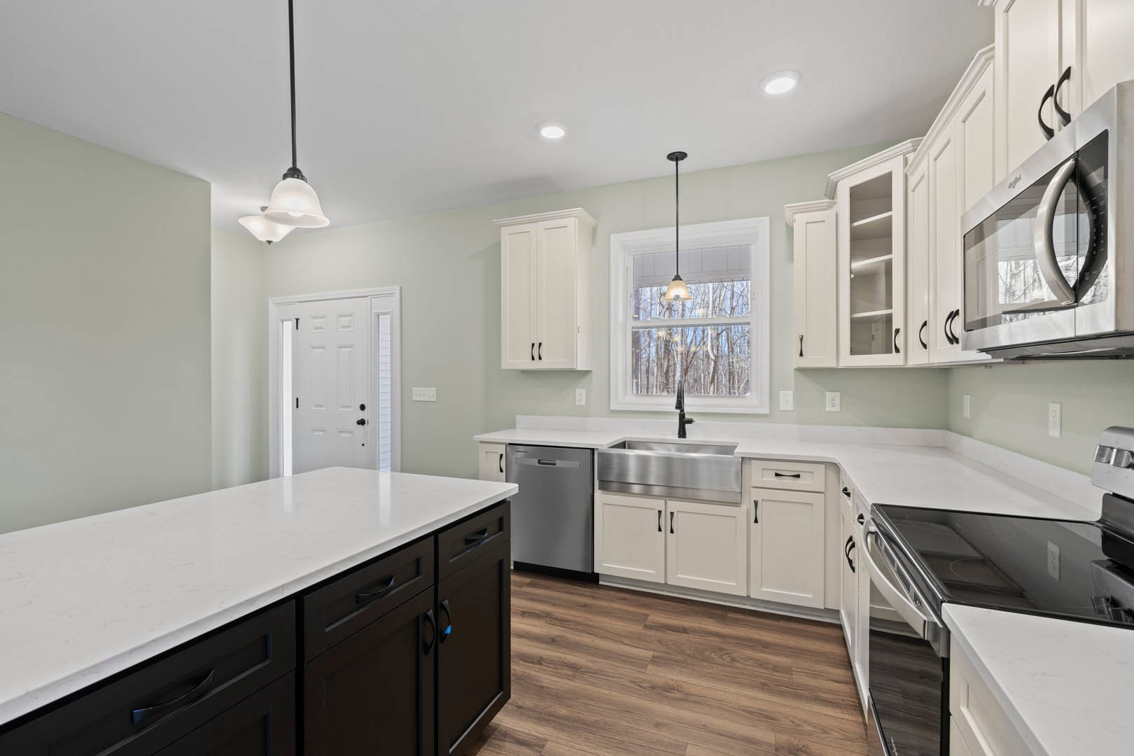 White kitchen cabinets with black appliances, quartz countertop, stainless steel sink, overhead light fixture, and a white door featuring black hardware