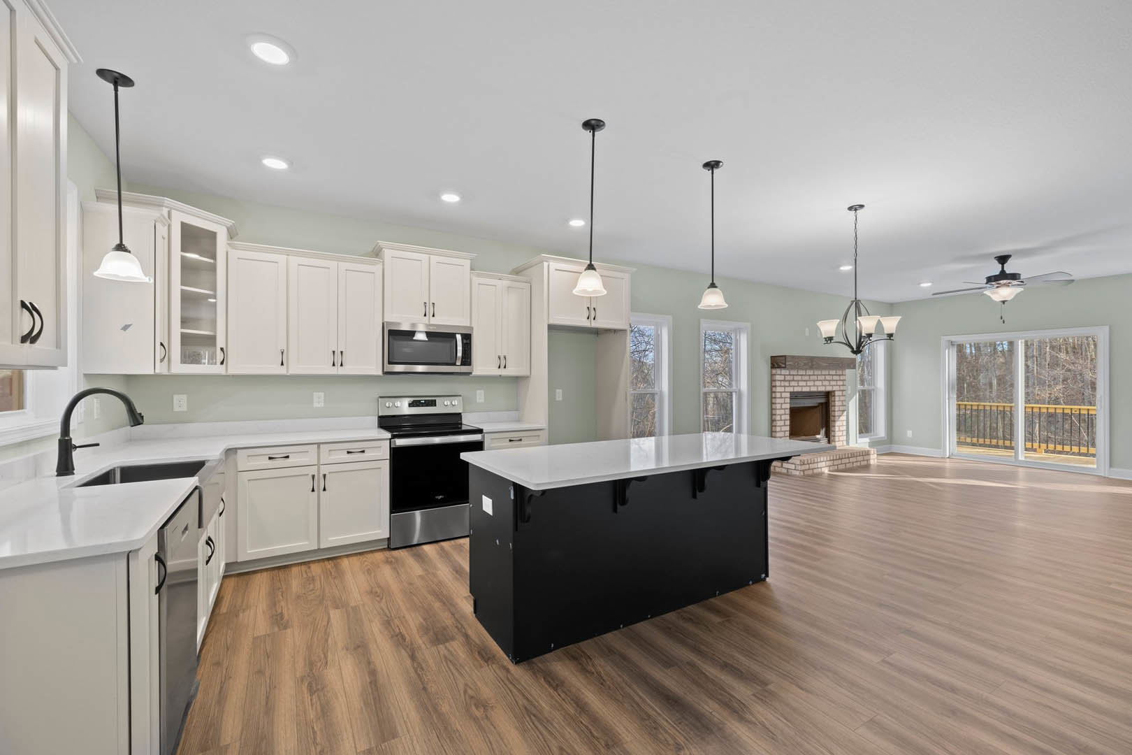 Spacious kitchen featuring a large island with black and white countertop, stainless steel dishwasher, blurred microwave, modern cabinetry, close-up light fixture, and window