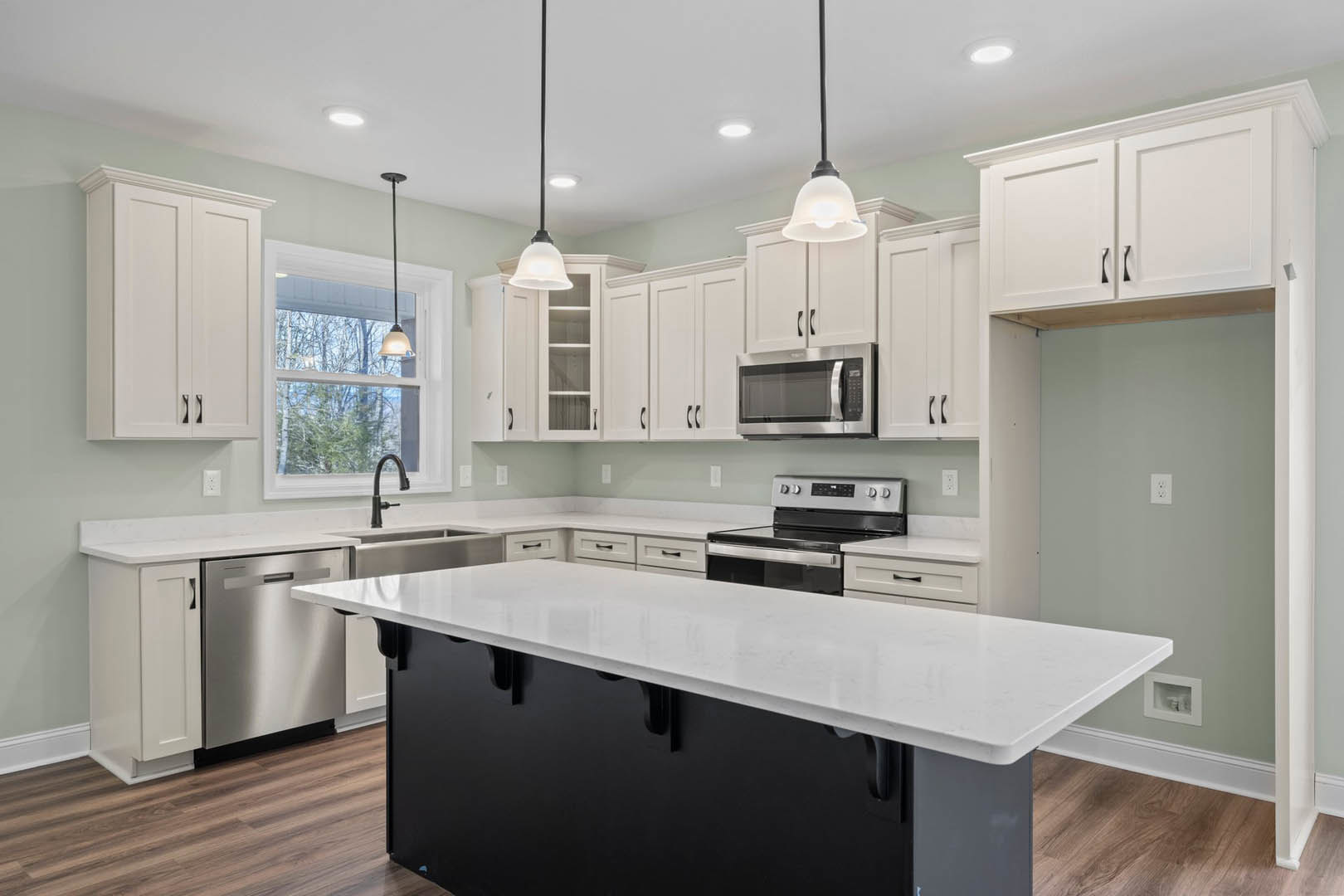 White kitchen cabinets and black island with white countertop, stainless steel stove, microwave, dishwasher, and window providing natural light