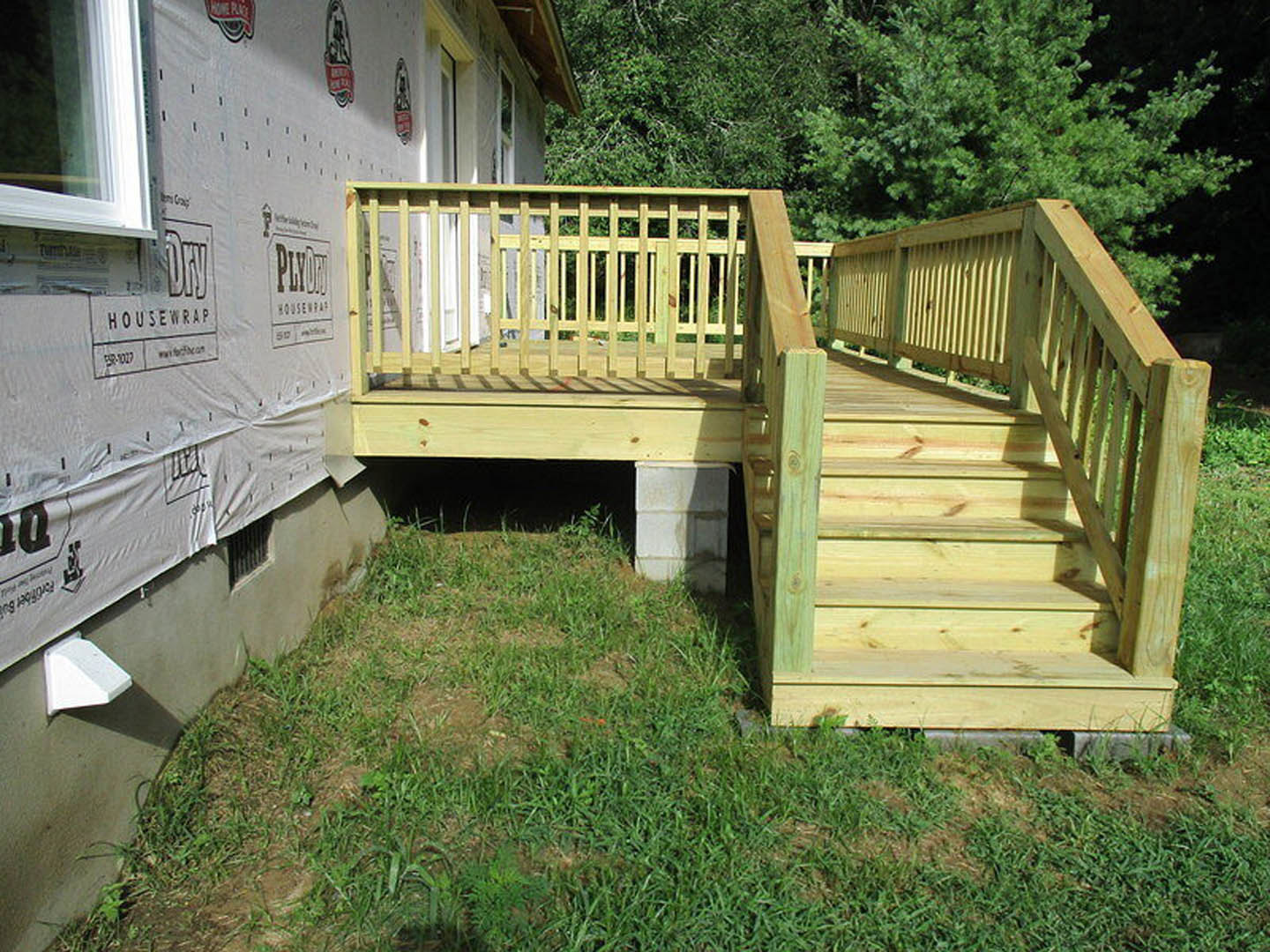 Wooden deck with railings attached to house, overlooking grassy backyard and surrounded by trees