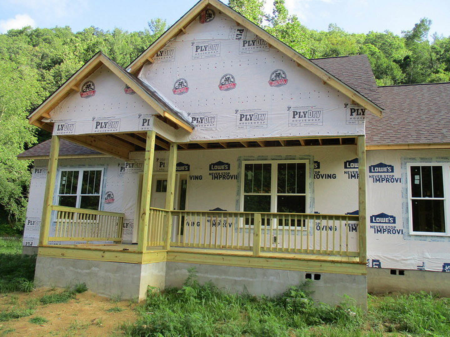 Two-story home with covered front porch, white-framed windows, gray siding, and landscaped yard with trees