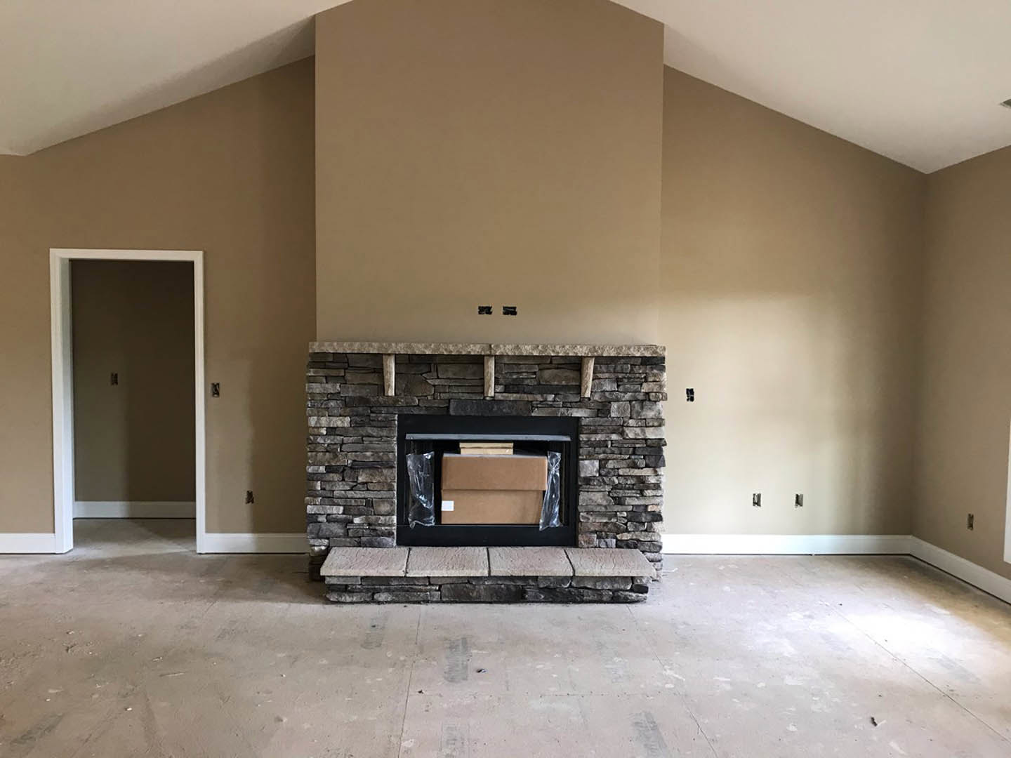 Modern living room with concrete floor, stone step, wood-burning stove set in a fireplace, built-in shelves, and a door with a light switch.