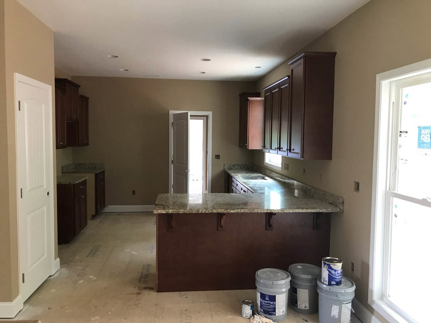 Marble kitchen countertop with scattered paint cans, white cabinetry, stainless steel sink, and a partially painted wall