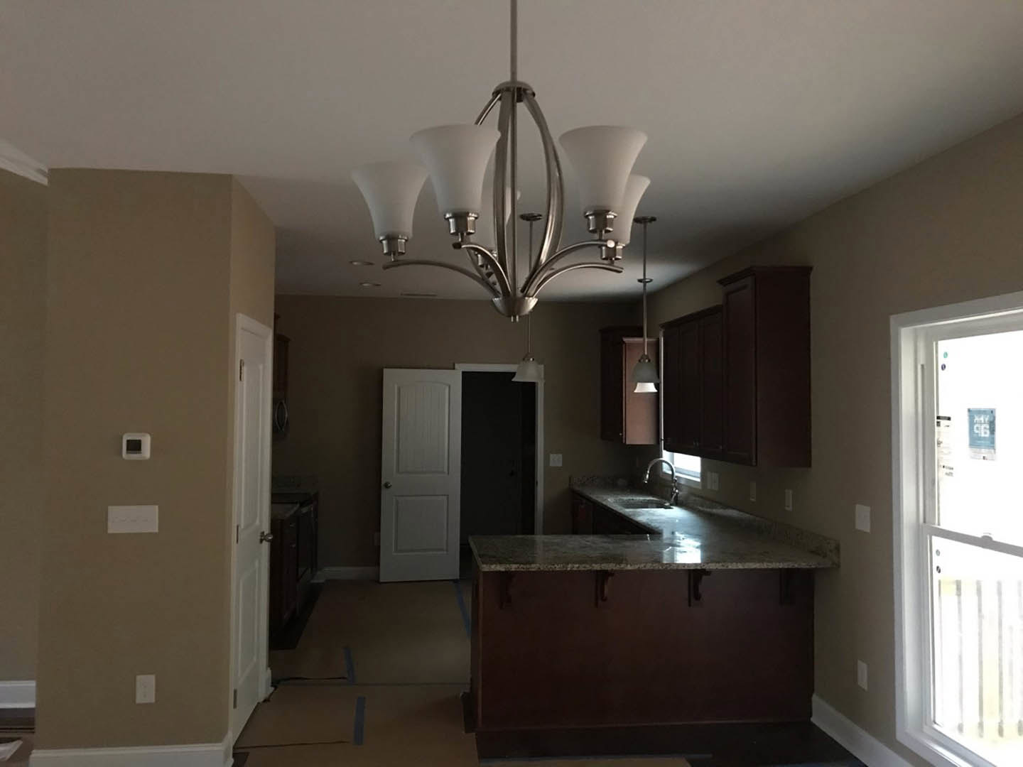 Kitchen with white cabinetry, marble countertop and undermount sink, four-shade chandelier above island, stainless steel appliances, white door with silver knob, window letting in