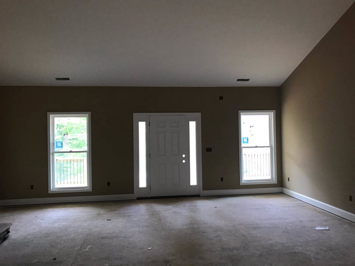 Bright room with white paneled door, two large windows with white frames, light-colored flooring, and smooth white walls.