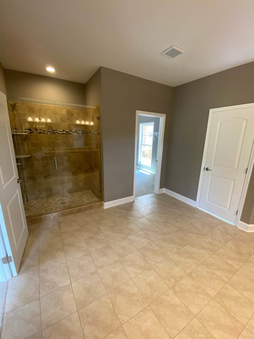 Bathroom featuring a glass shower enclosure, gray tile flooring, white door with silver handle, and window allowing natural light.
