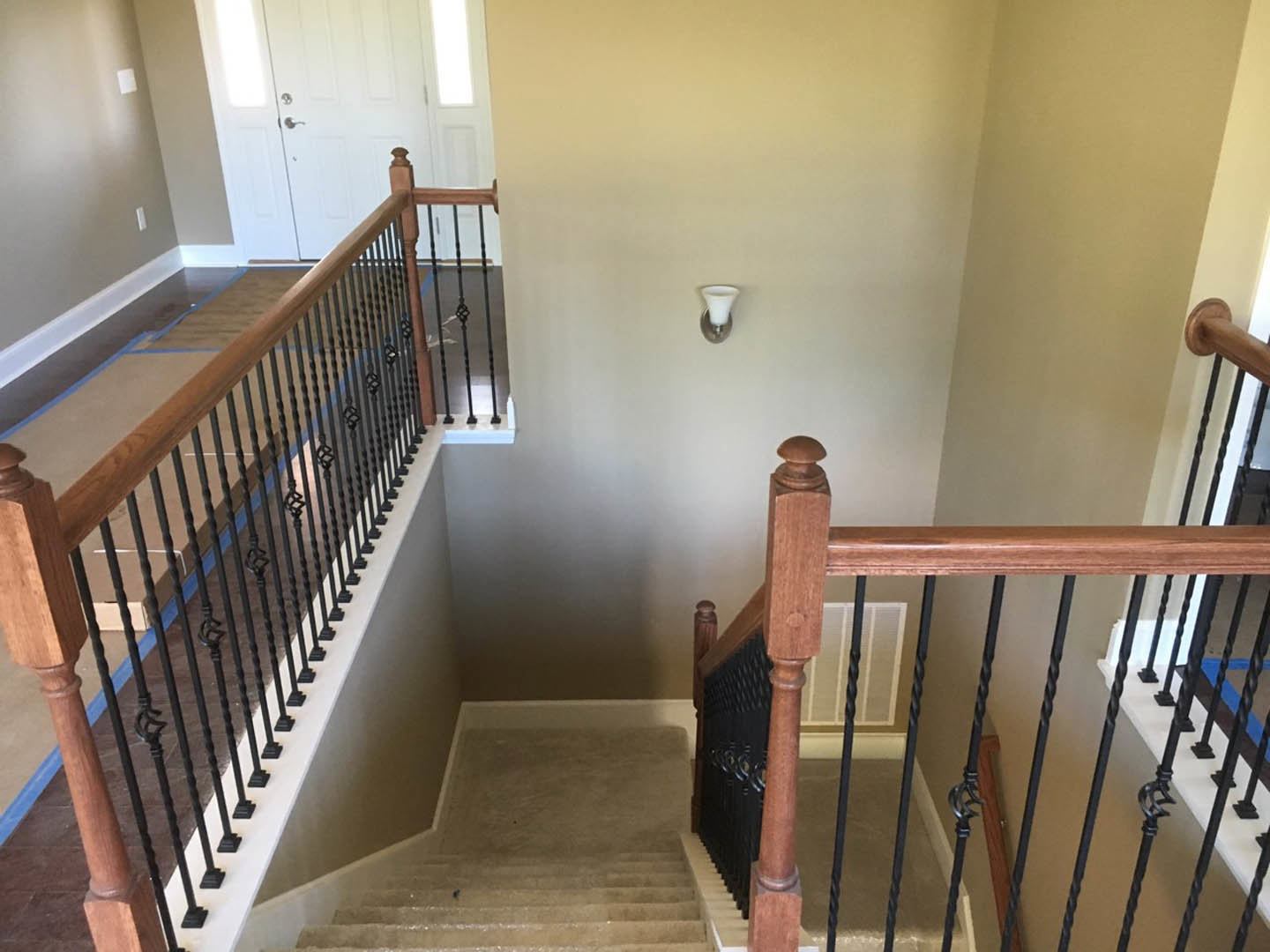 Staircase with black metal railing, light wood steps, white walls, and a modern pendant light with a white shade