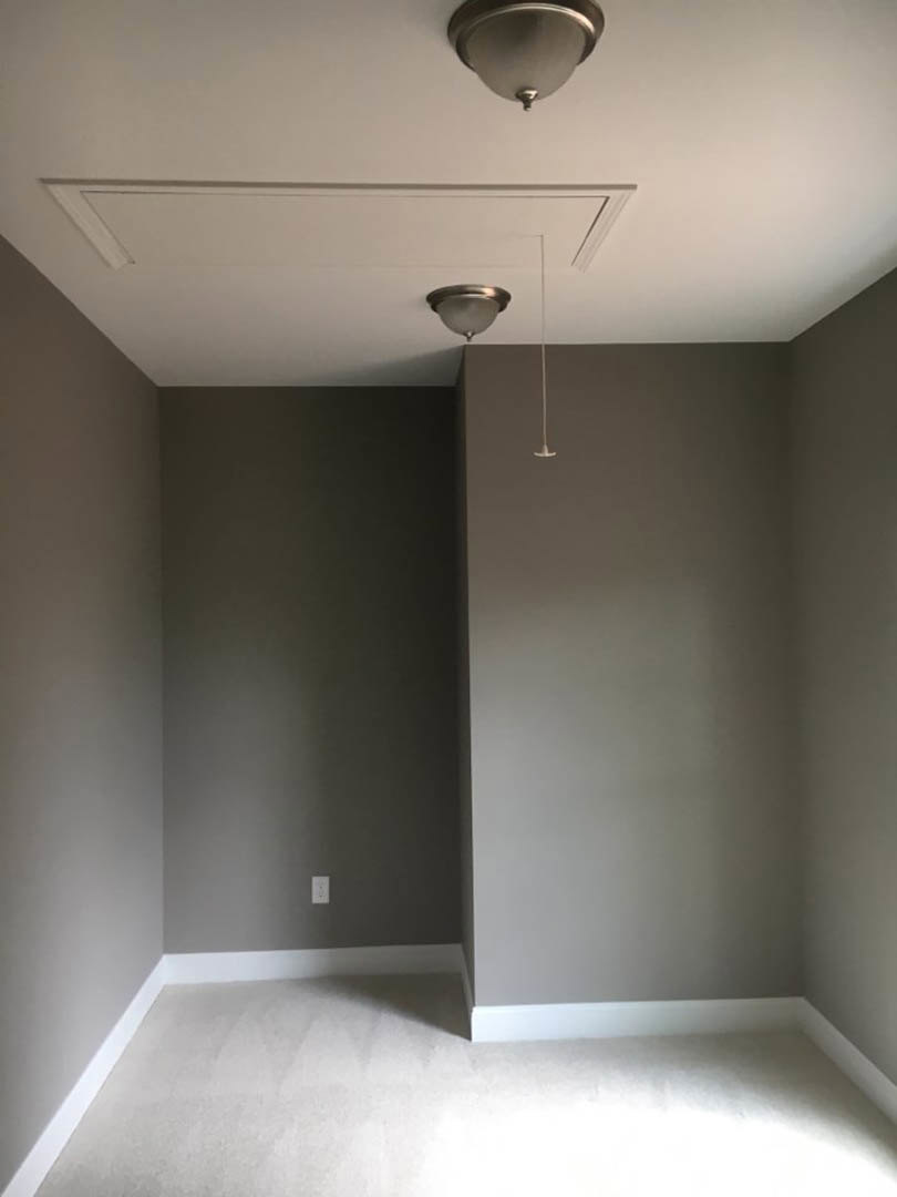 White carpeted floor with white baseboard, grey plaster wall, and modern ceiling light fixture in a residential interior.