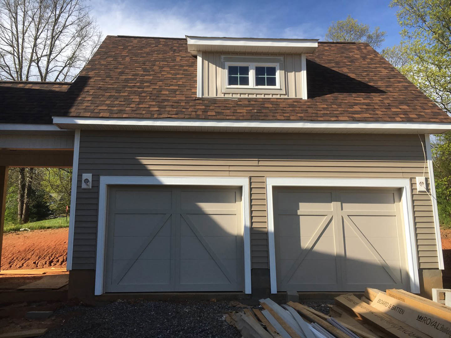 White garage with two paneled doors, white trim, and adjacent windows under a gabled roof; blue sky and trees in background.