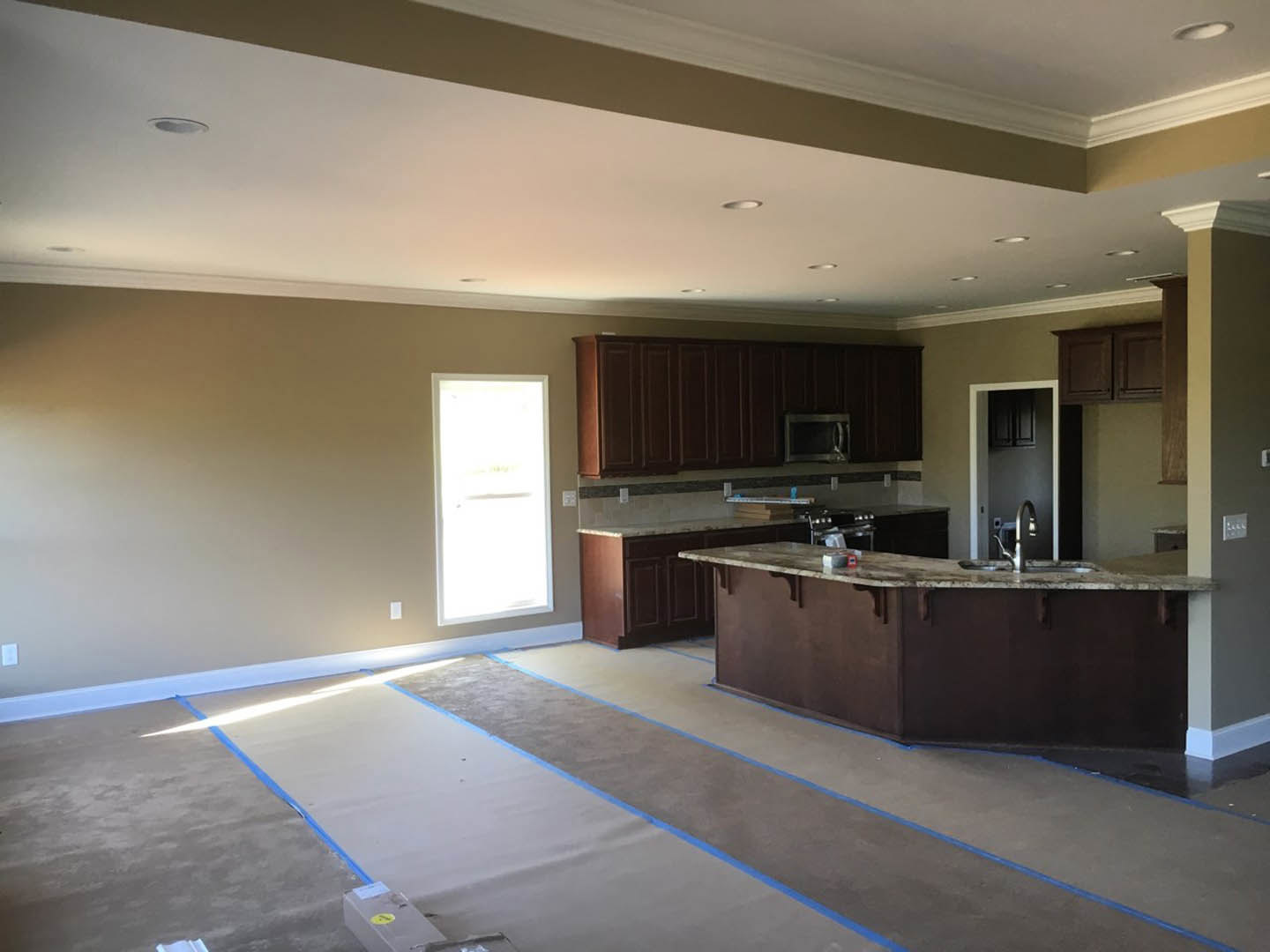 Open-concept kitchen featuring a bar-height counter with sink, white cabinetry, built-in microwave, white door illuminated by natural light, and light-colored flooring marked with
