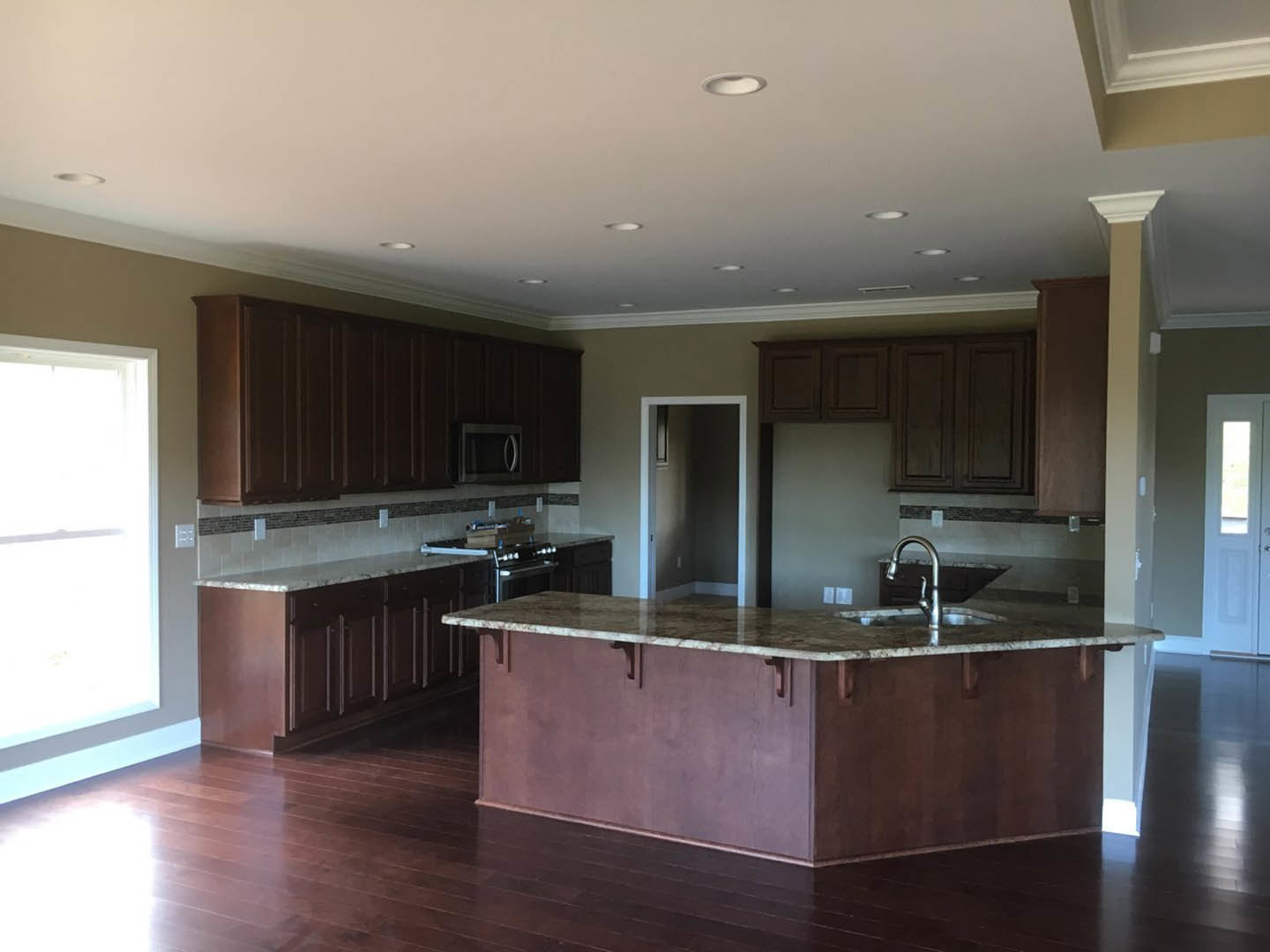 Spacious kitchen featuring a large central island with built-in sink, dark brown cabinetry, light countertops, and a white door with window; doorway displays framed artwork on