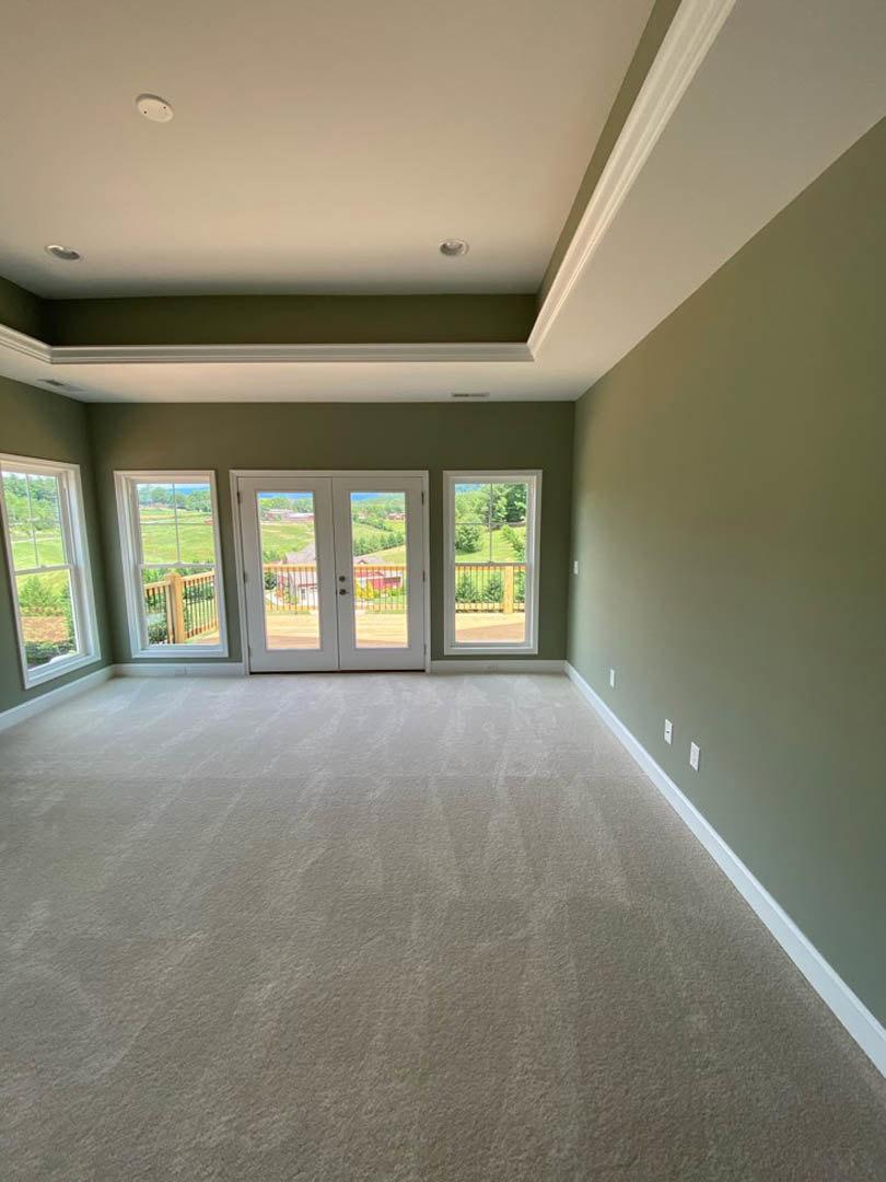 Carpeted room featuring double glass-paneled doors and large windows overlooking a green field, with white walls and ceiling.