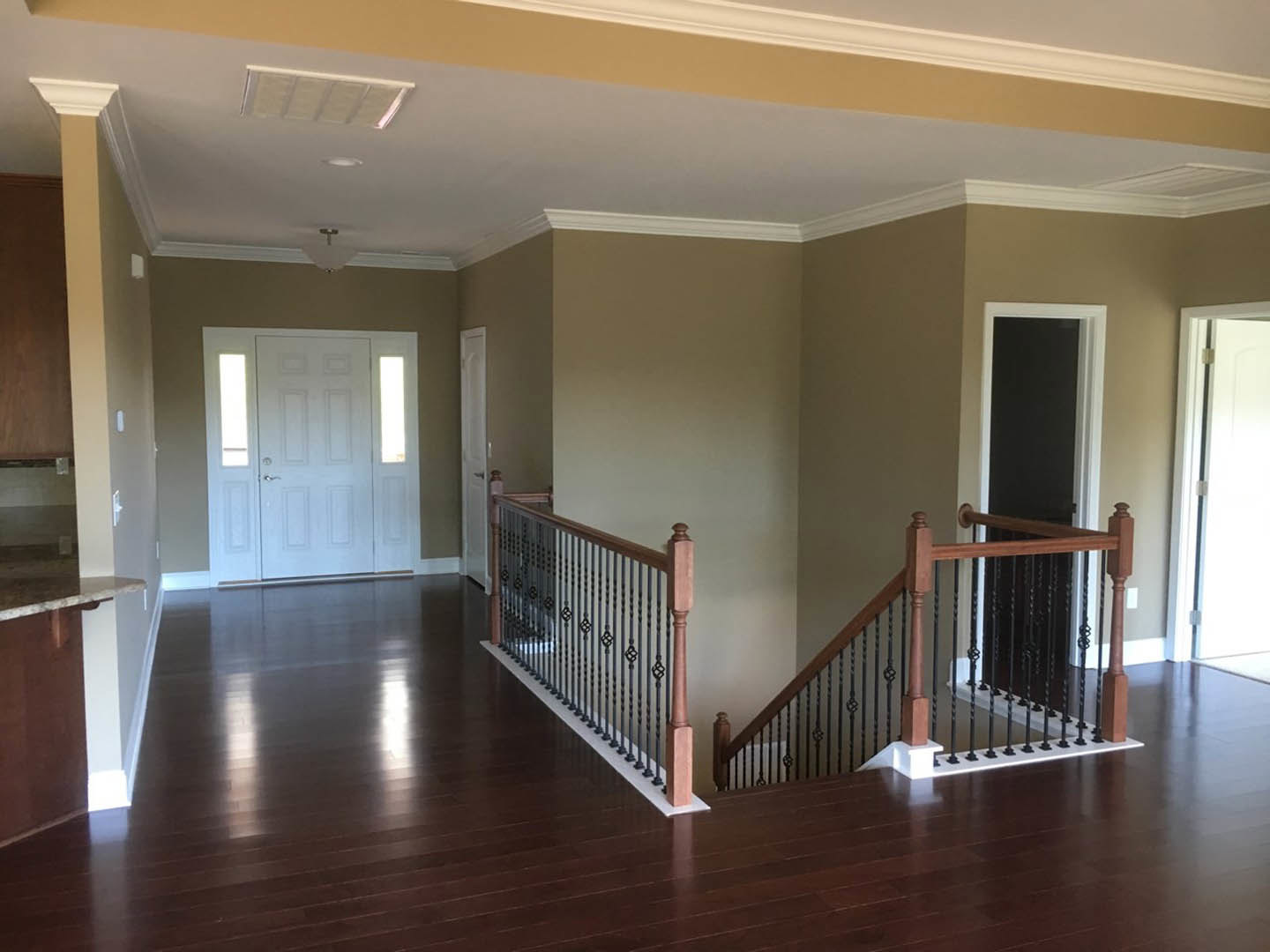 Hallway featuring laminate wood flooring, white walls, a staircase with wooden handrail, and a white door with two glass windows