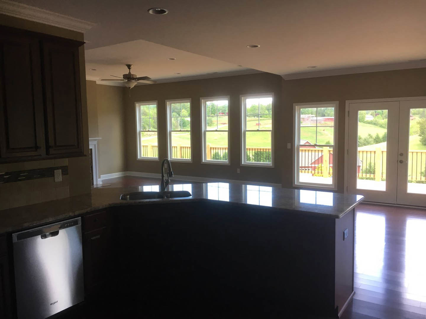 Modern kitchen with white cabinetry, stainless steel dishwasher, glossy tile flooring, large windows overlooking green lawn and balcony with metal railing