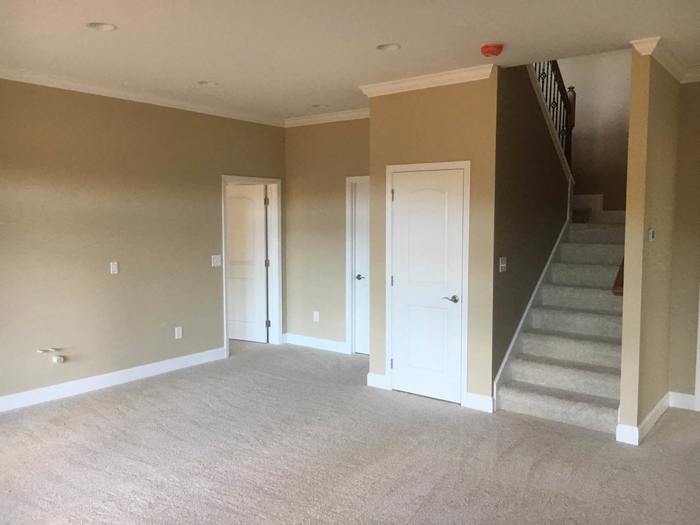 Carpeted room with white walls, white door featuring a silver handle, staircase with wooden steps, ceiling with recessed lighting