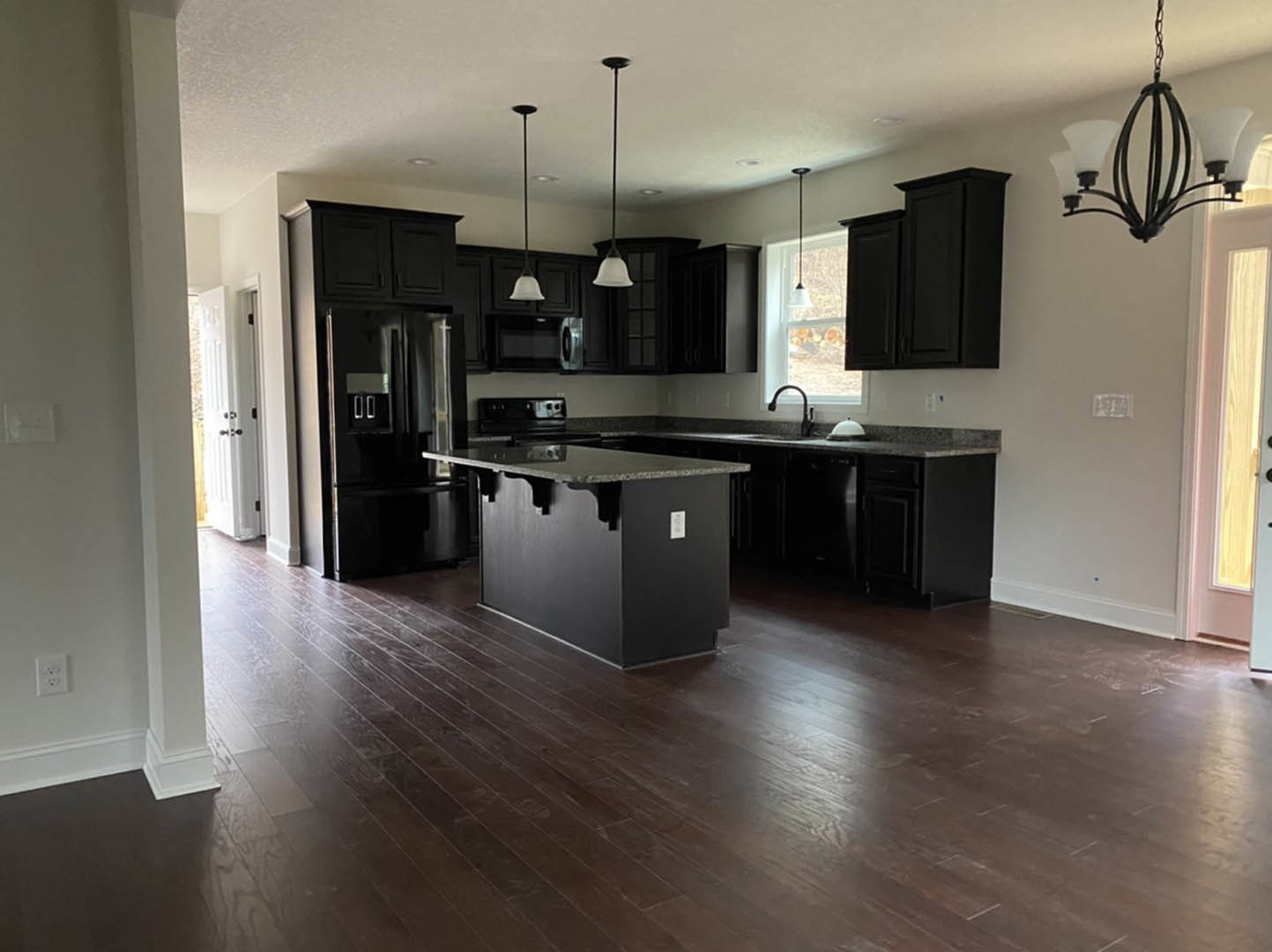 Kitchen with matte black cabinets, matching black island topped with white marble, tile flooring, stainless steel sink, and modern chandelier overhead