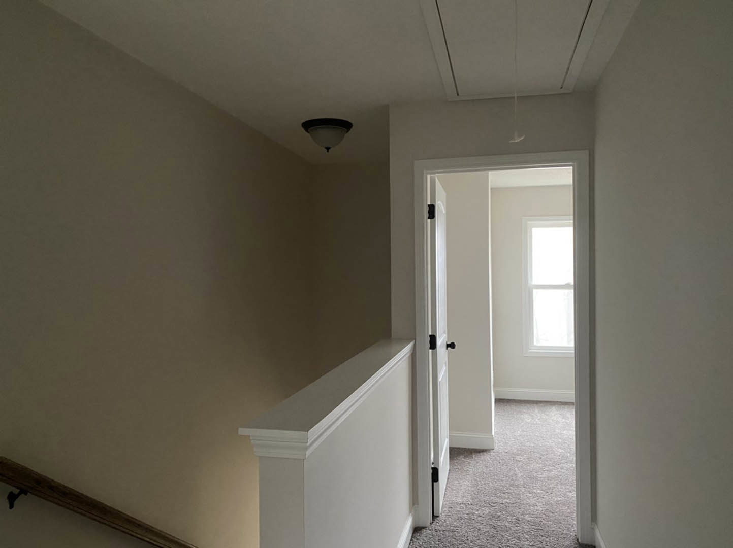 Hallway with white plaster walls, white base molding, carpeted floor, white door, and window letting in natural light