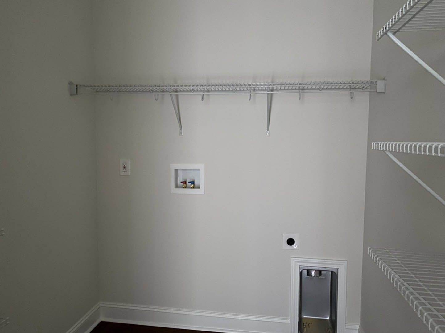 White plaster wall with built-in shelves, metal object centered between shelves, light wood floor, and white ceiling.