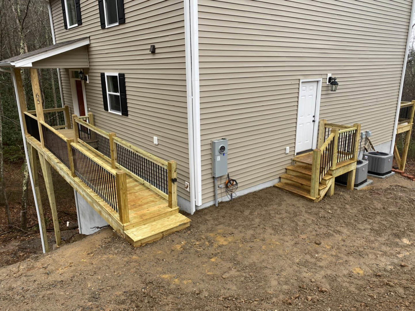 Wooden deck with railings and stairs leading to a white door, white-framed window, and antenna on the exterior of a house