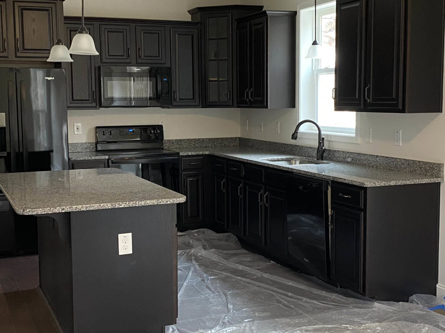 Kitchen with matte black cabinets, speckled granite countertops, stainless steel appliances, white electrical outlet, and plastic sheeting covering the floor