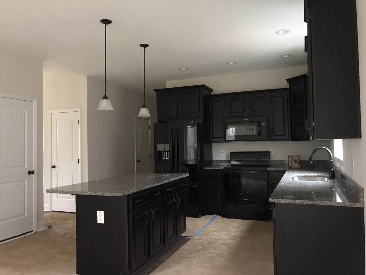 Kitchen with matte black cabinets, granite countertops, stainless steel appliances, white walls, and a black kitchen island.