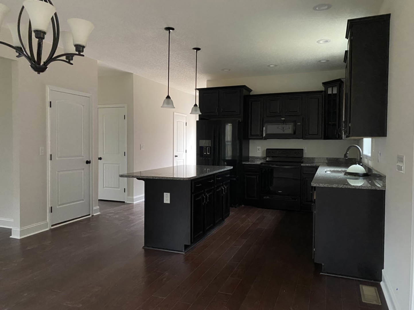 Kitchen with matte black cabinets, wood plank flooring, marble-topped island, black stove, white door with black hardware, and modern chandelier