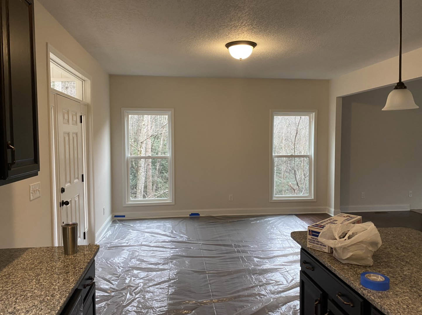 Kitchen under renovation with plastic sheeting covering laminate flooring, white walls, a long pole leaning against the wall, countertop partially visible, metal container on the