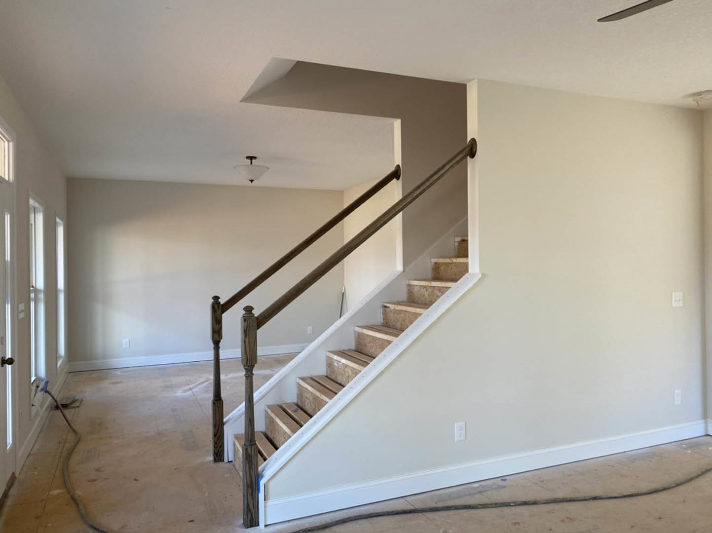 Wood staircase with matching handrail, plaster walls, ceiling-mounted light fixture, and metal object resting on hardwood floor