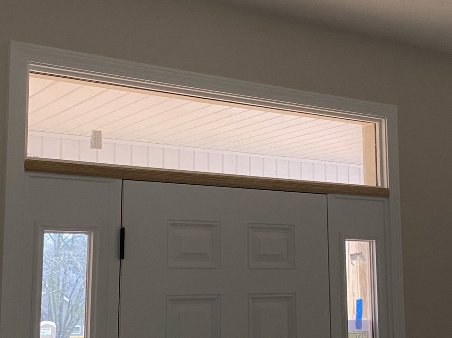 White double entry doors topped by a rectangular transom window, surrounded by white molding and wall, with silver door handles and natural daylight filtering in.