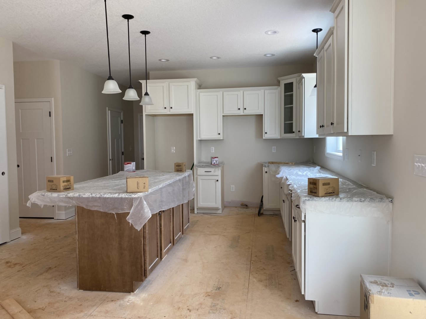 Kitchen with white shaker cabinets, black handles, light countertops, and a table covered in protective plastic with moving boxes