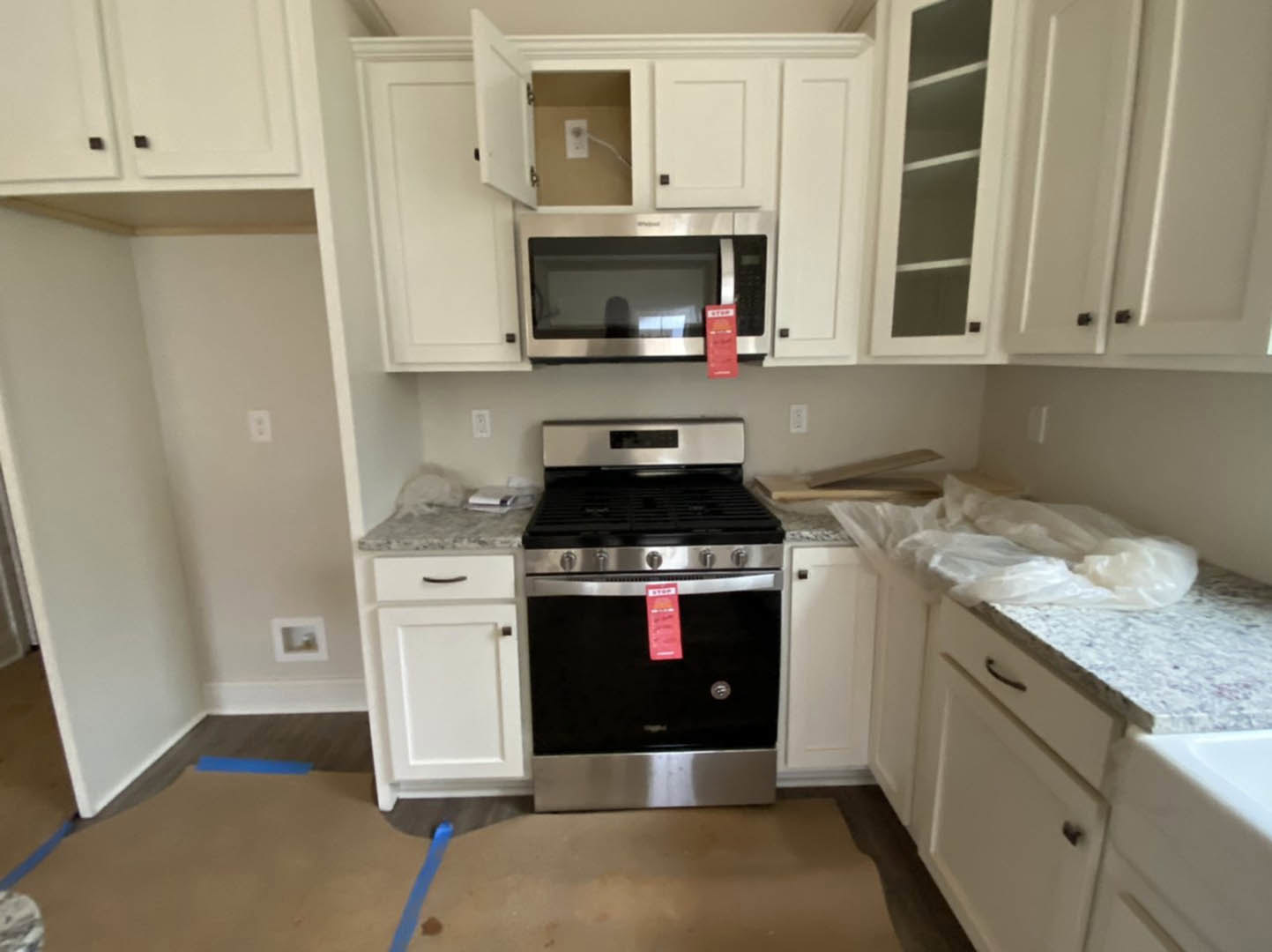 White shaker cabinets, stainless steel microwave above black and silver stove, light stone countertops, red box on counter, window with white trim